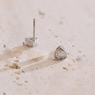 Heart-shaped silver earring with clear gemstone on a beige surface