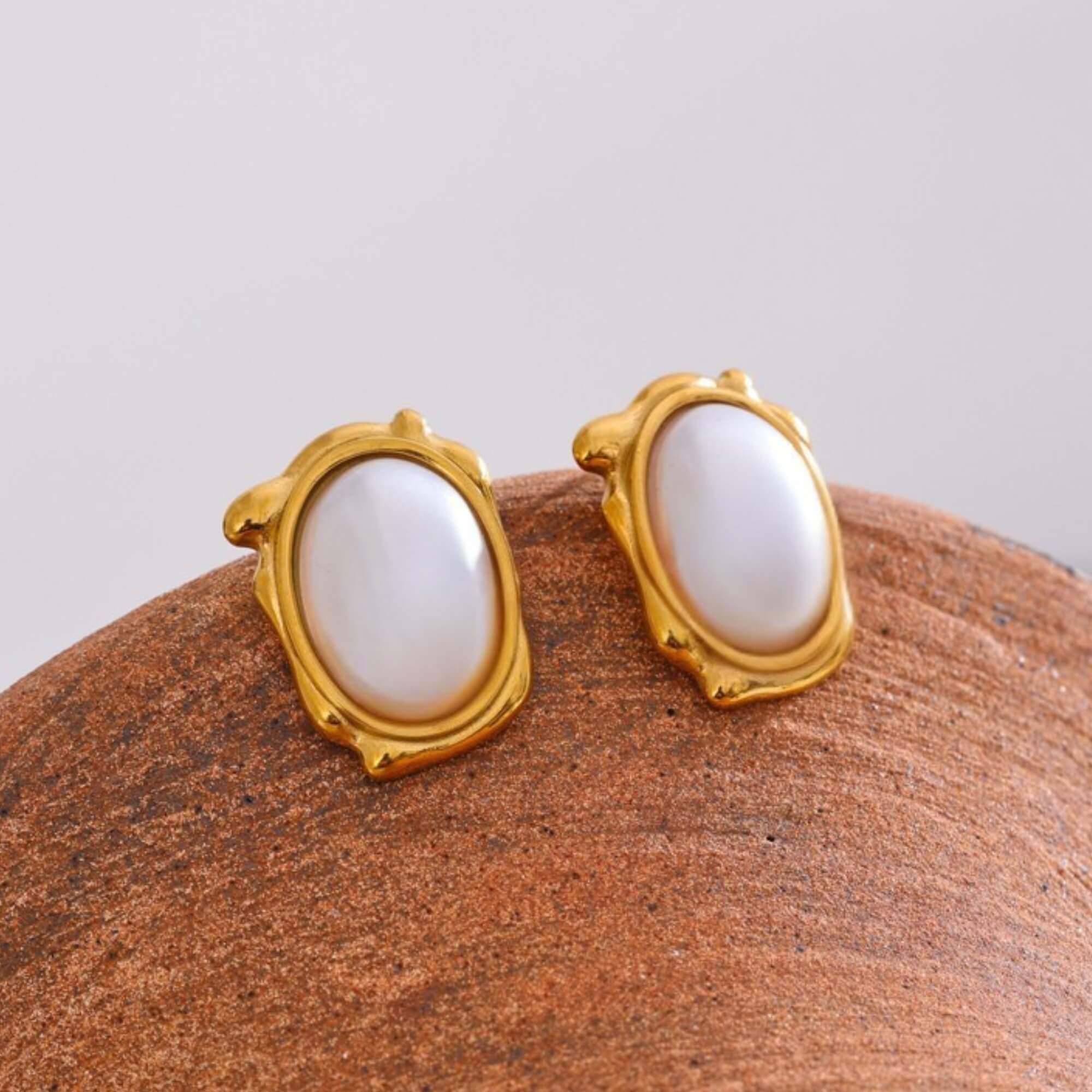 Gold-framed earrings with white stones on a brown surface